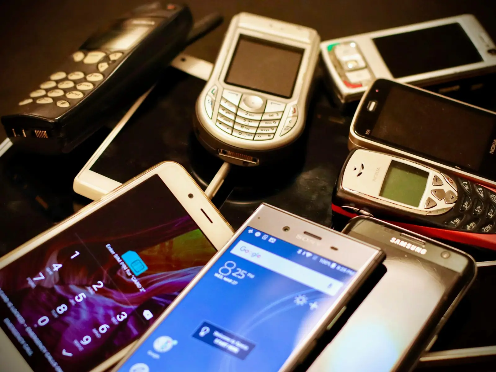 Vários celulares de marcas e épocas diferentes empilhados sobre uma mesa