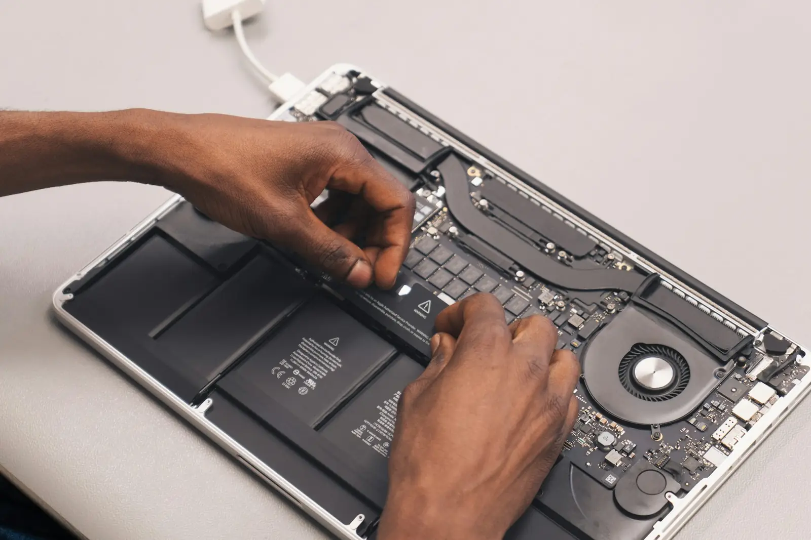 Mãos de um técnico trabalhando dentro de um notebook aberto, com a bateria e a placa à mostra